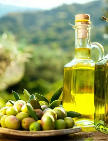 Garrafa de vidro com azeite de oliva dourado ao lado de um ramo de oliveira e azeitonas frescas.